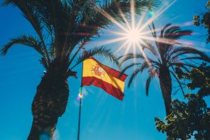 Big Spanish flag, palm trees, sun and blue sky.